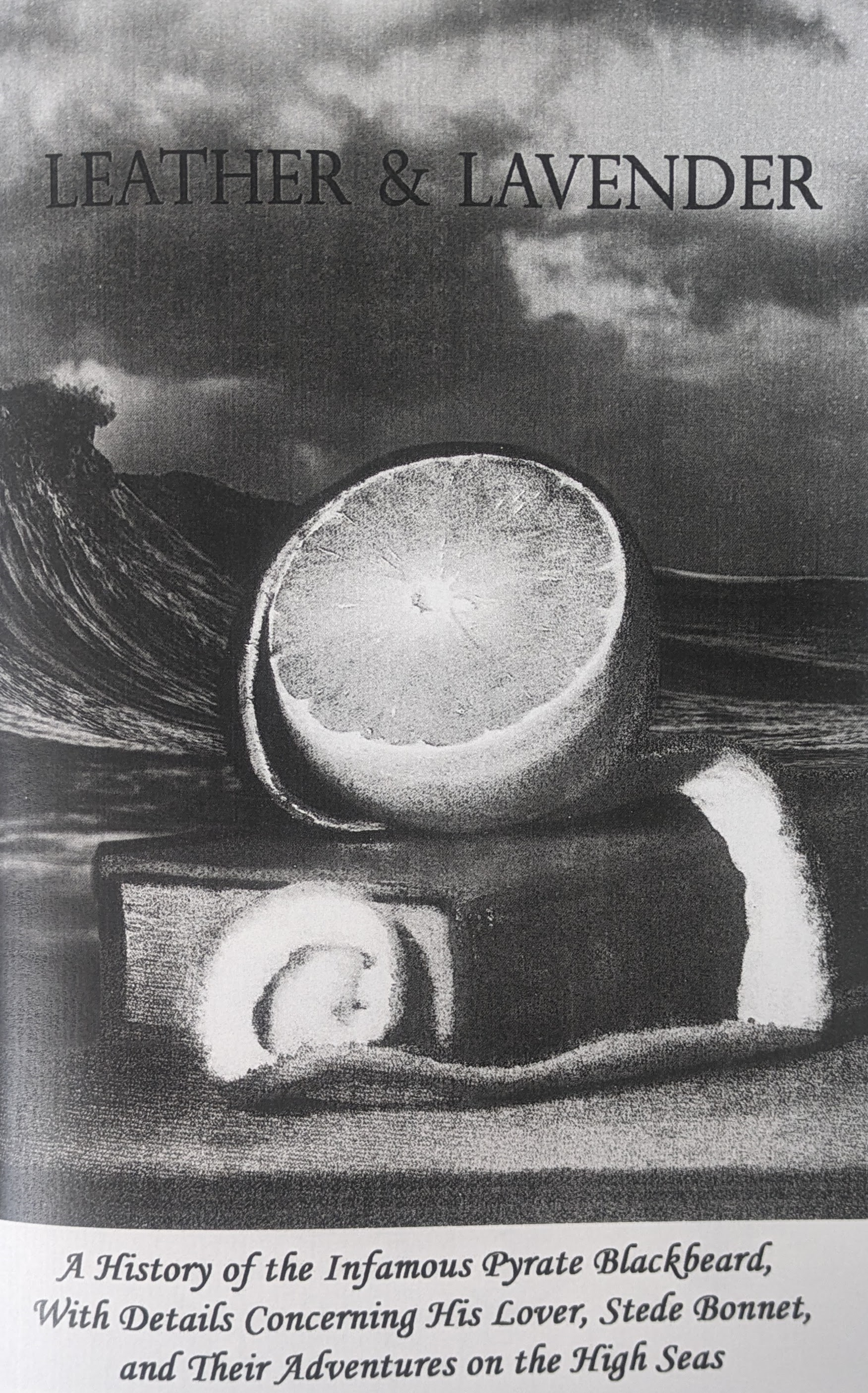 The cover of the zine “Leather and Lavender.” A half-peeled orange sits atop a leather book. In the background is the sea.